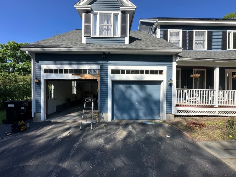 Blue garage door installation in progress on colonial home with ladder visible